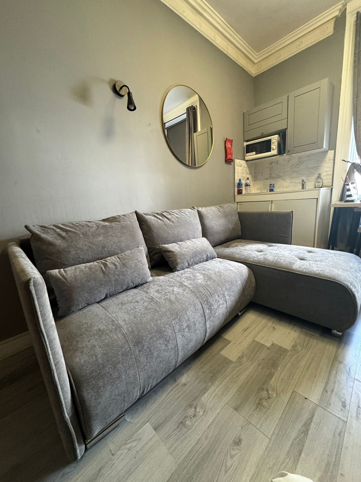 A grey sectional sofa with a round mirror and a microwave above it.