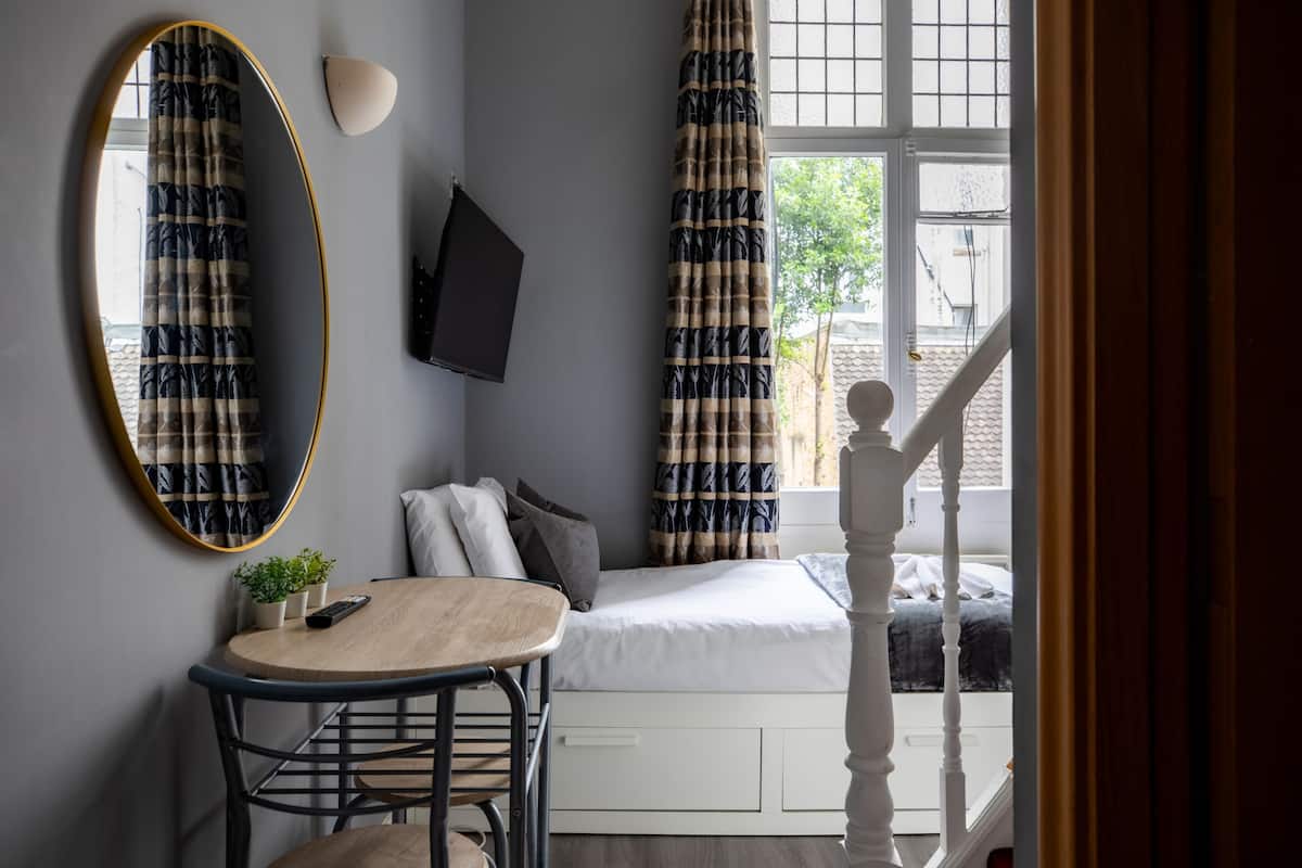 Un dormitorio con cama, una mesa redonda con sillas, televisor y ventana con cortinas.