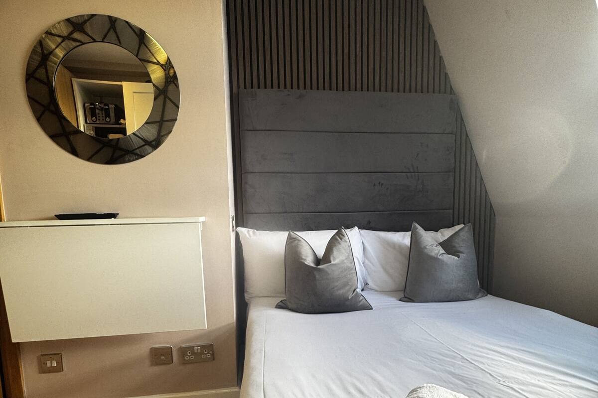 Una habitación de hotel moderna con una cama grande, un espejo redondo y un cabecero de madera.