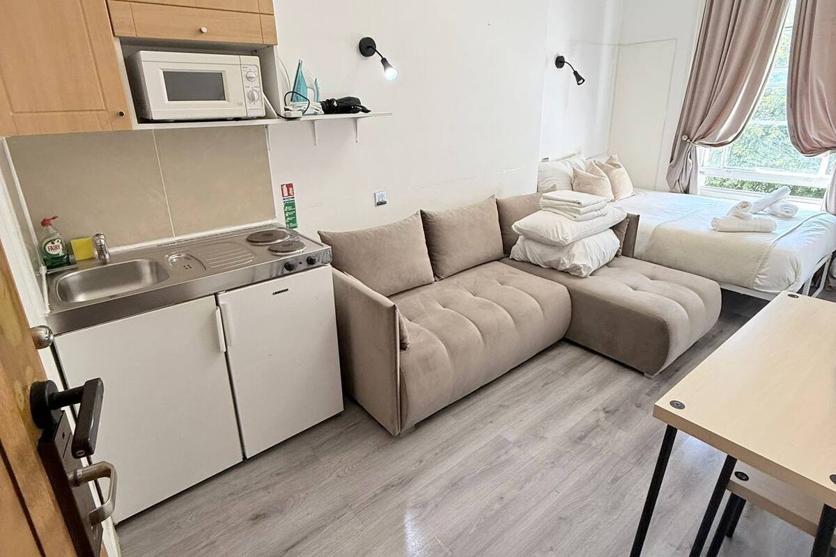 Un espacio habitable compacto con kitchenette, sofá cama, mesa de comedor y ventana con cortinas.