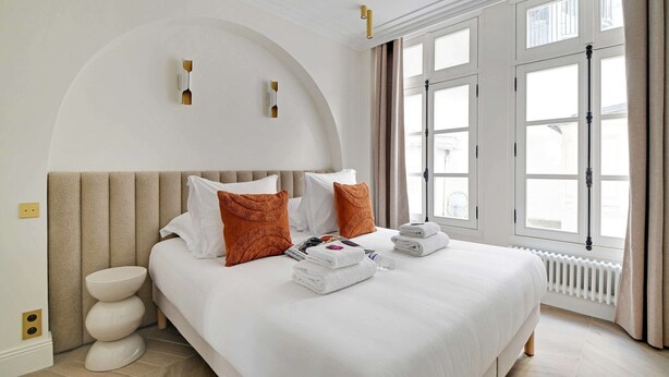Ein Hotelzimmer mit einem großen Bett, zwei Kissen, einem Nachttisch und einem Fenster mit Vorhängen.