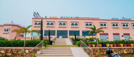 Un bâtiment rose avec une enseigne indiquant « Restaurant Raso » et « Hôtel de l’aéroport ».