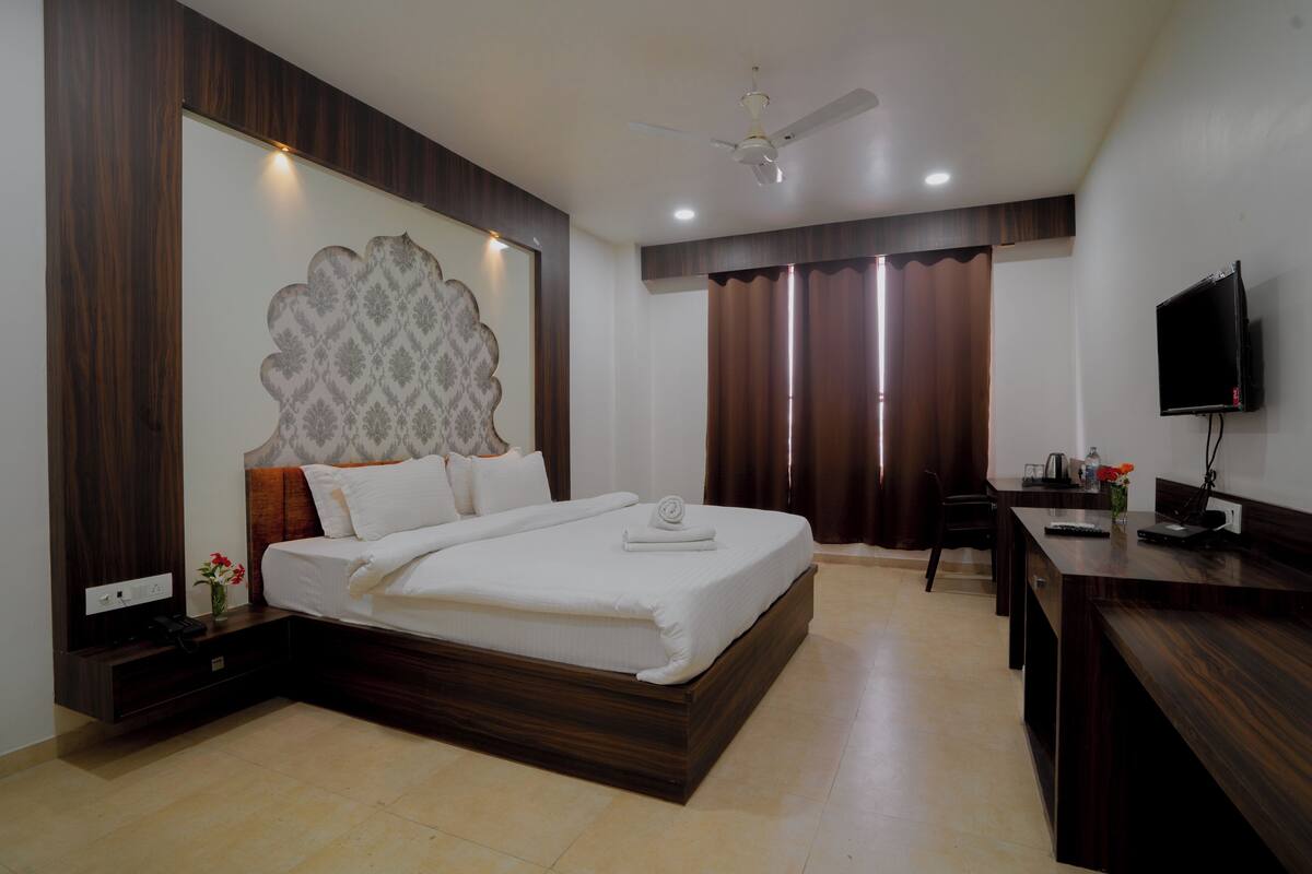 Quarto de hotel com uma cama grande, escrivaninha, televisão e ventilador de teto.