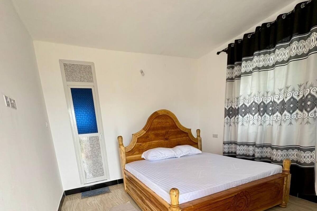 Un dormitori amb llit de fusta, finestra amb tonalitat blava i cortines estampades.