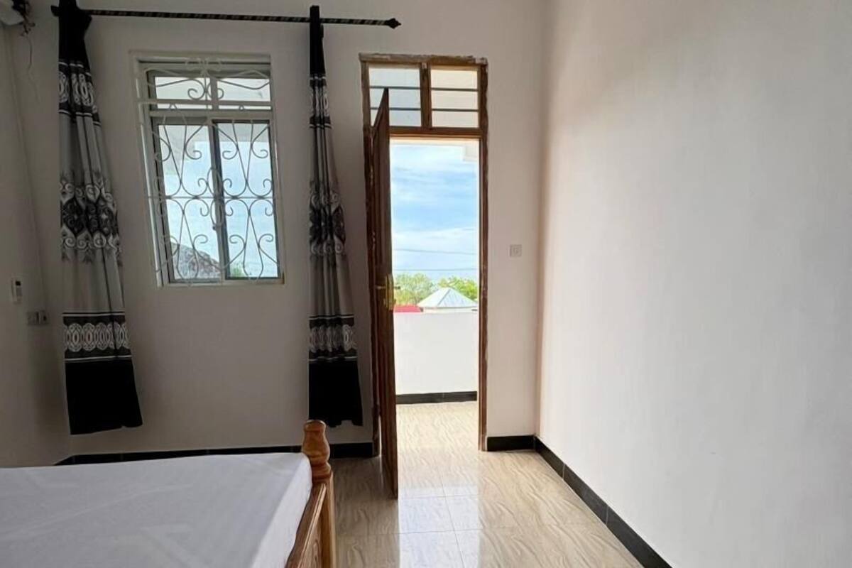 Un dormitori amb llit de fusta, una finestra amb cortines decoratives i vista cap a l'exterior.
