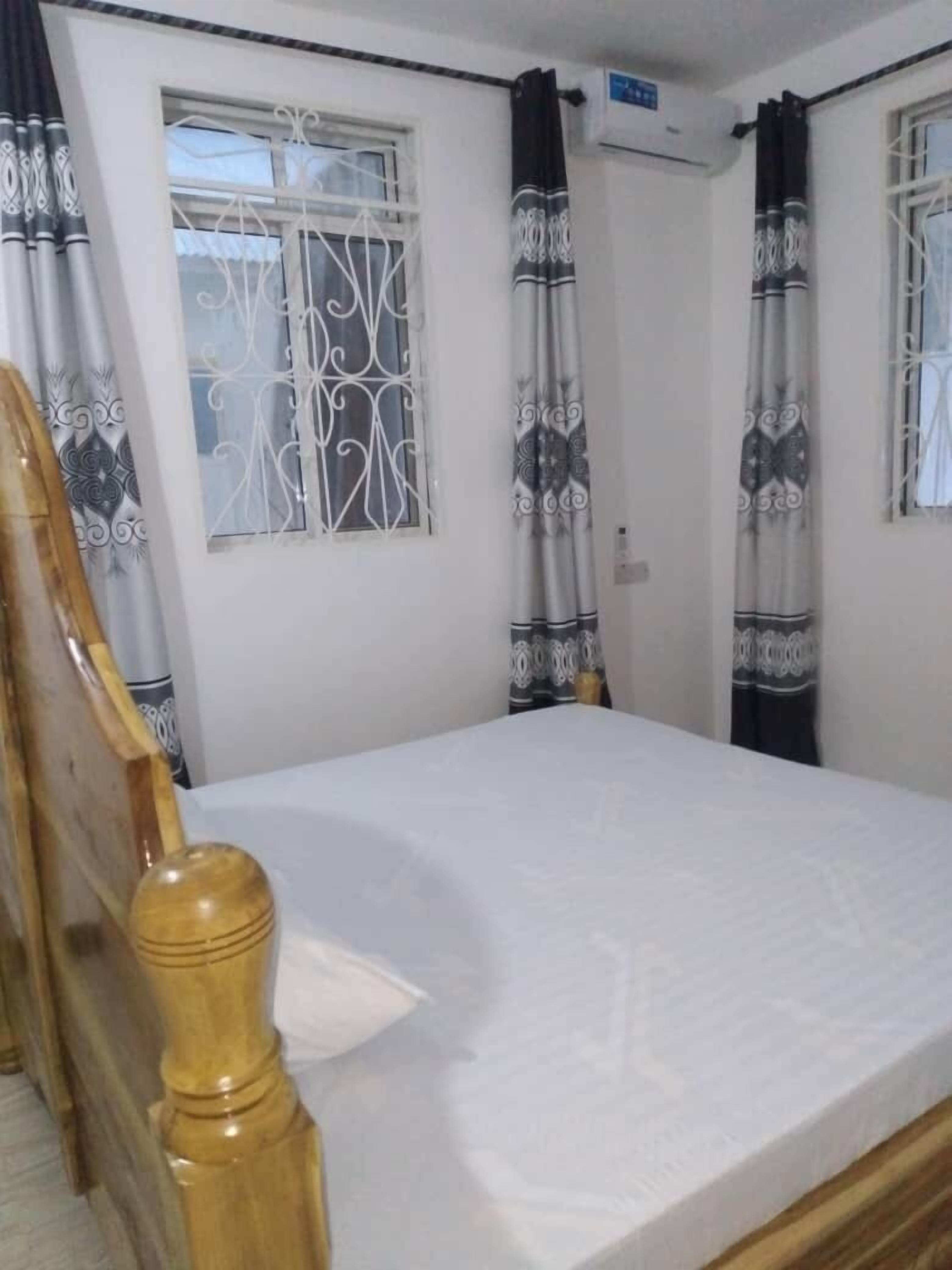 A bedroom with a wooden bed frame, a window with decorative metal bars, and patterned curtains.