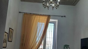 A room with a chandelier, a sofa, a window with curtains, a potted plant, and a flat-screen TV. - Aurora Center City (Palermo)