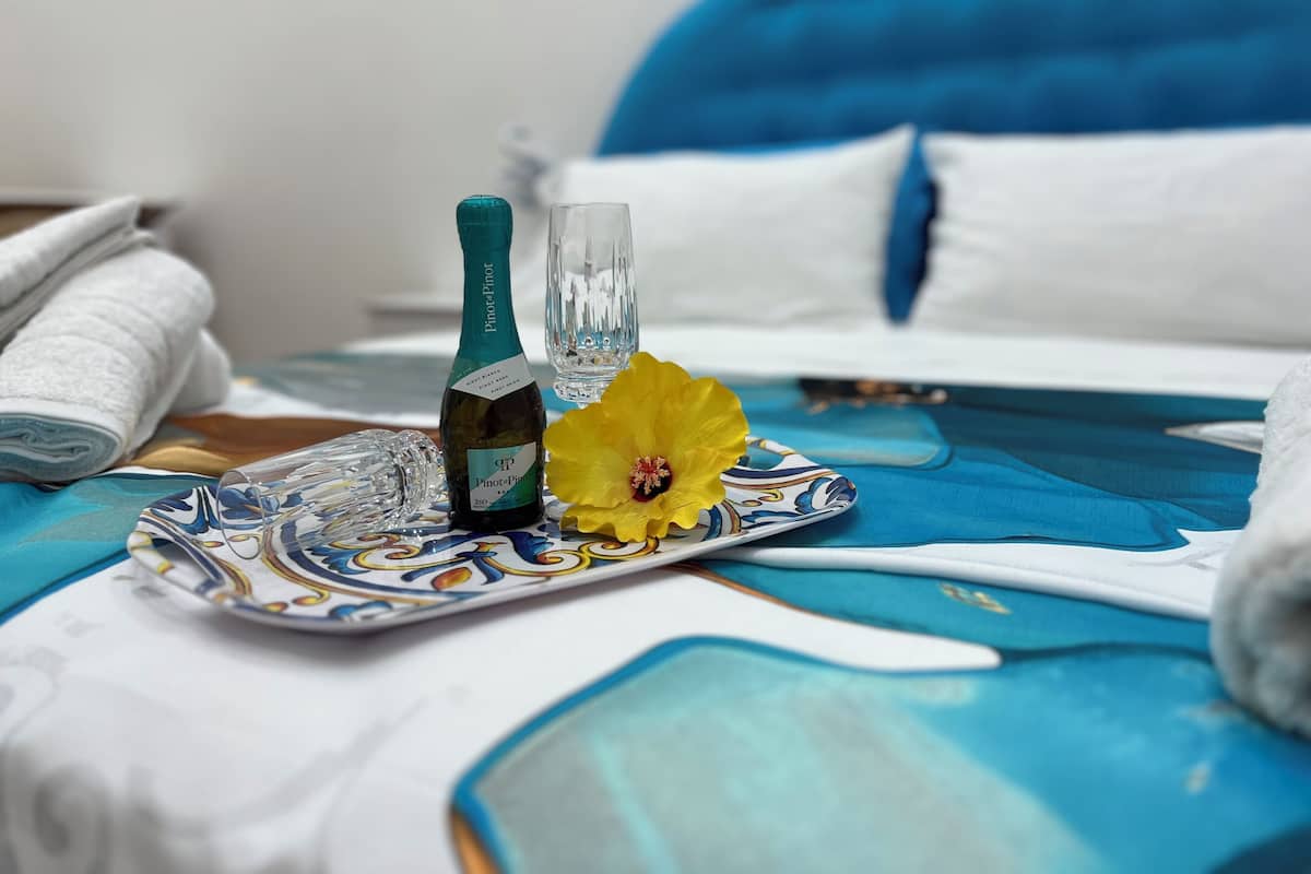 A bed with a blue headboard, a bottle of wine, a glass, and a yellow flower on a decorative tray.