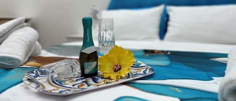 A bed with a blue headboard, a bottle of wine, a glass, and a yellow flower on a decorative tray.