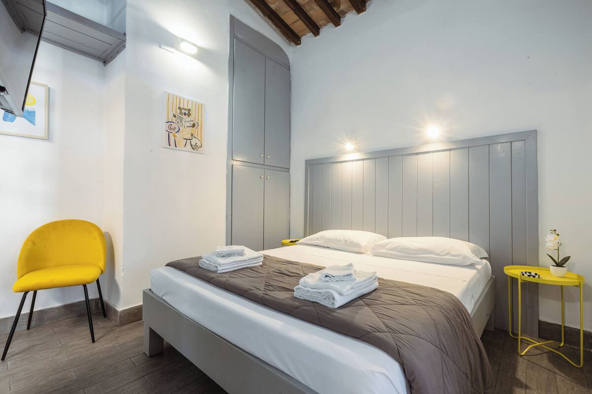 A neatly arranged bedroom with a bed, a chair, and a small table with a plant.