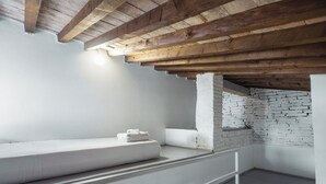 A modern, minimalist room with a white bed, a brick accent wall, and exposed wooden beams. - Le Casine Firenze (Florence)