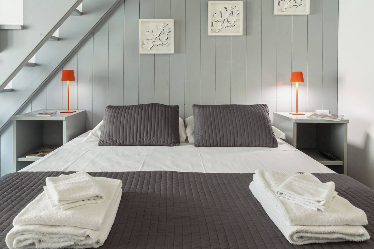 A modern bedroom with a bed, two nightstands, a staircase, and wall art.