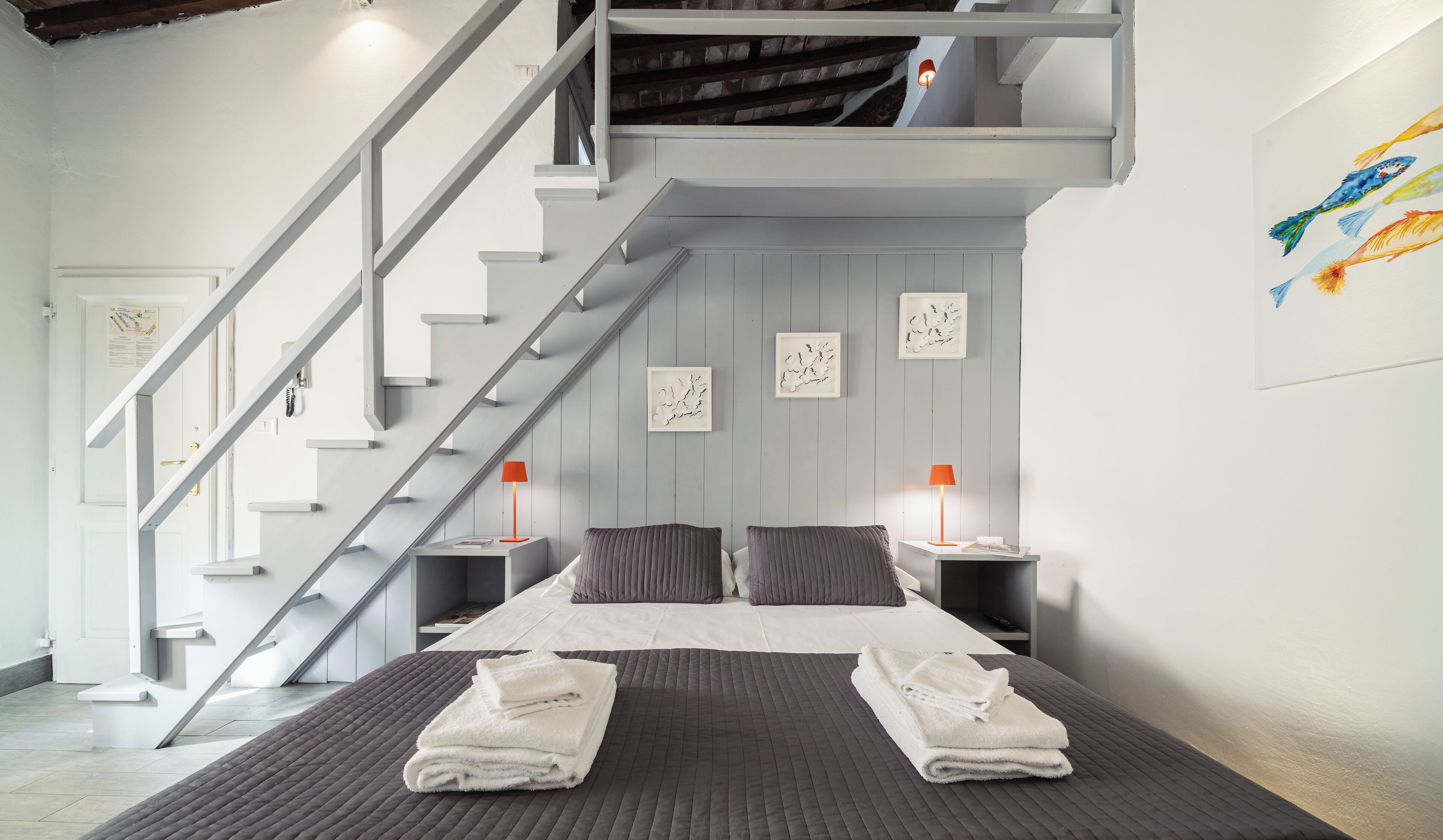 A modern bedroom with a large bed, two nightstands, a staircase, and artwork on the walls.