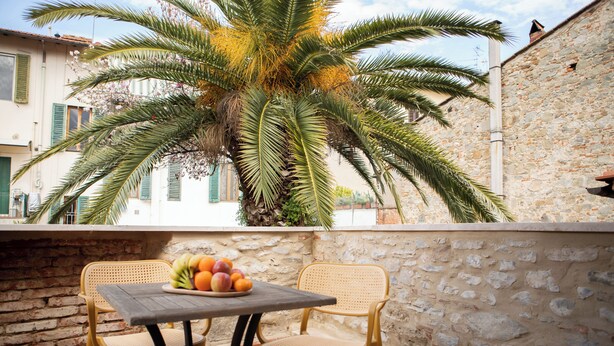 A balcony with two wicker chairs, a small table with a fruit bowl, and a palm tree. - Le Casine Firenze (Florence)