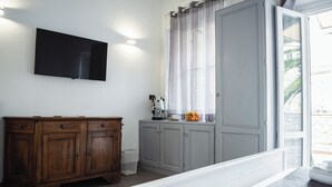 A room with a flat-screen TV mounted on the wall, a wooden cabinet, a window with curtains, and a bed with a white headboard. - Le Casine Firenze (Florence)