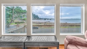 A room with three large windows offering views of a beach and forest.