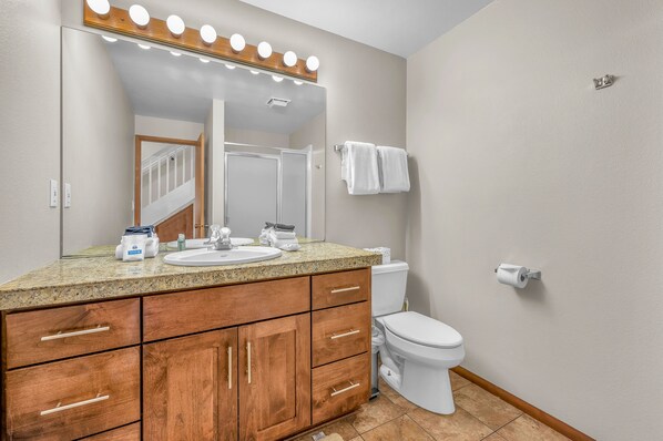 A bathroom with a vanity, sink, mirror with lights, toilet, and towel rack.