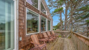 A wooden deck with Adirondack chairs, large windows, and a view of trees and buildings.