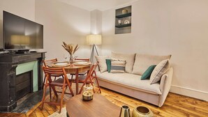 A living room with a sofa, a dining table with chairs, a TV, and a lamp. - Superb Apartment Le Marais/place des Vosges (Paris)