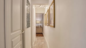 A hallway with framed pictures on the walls, a door on the left, and a sofa in the background. - Superb Apartment Le Marais/place des Vosges (Paris)