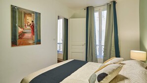 A hotel room with a bed, a painting on the wall, a door leading to a balcony, and a window with curtains. - Superb Apartment Le Marais/place des Vosges (Paris)