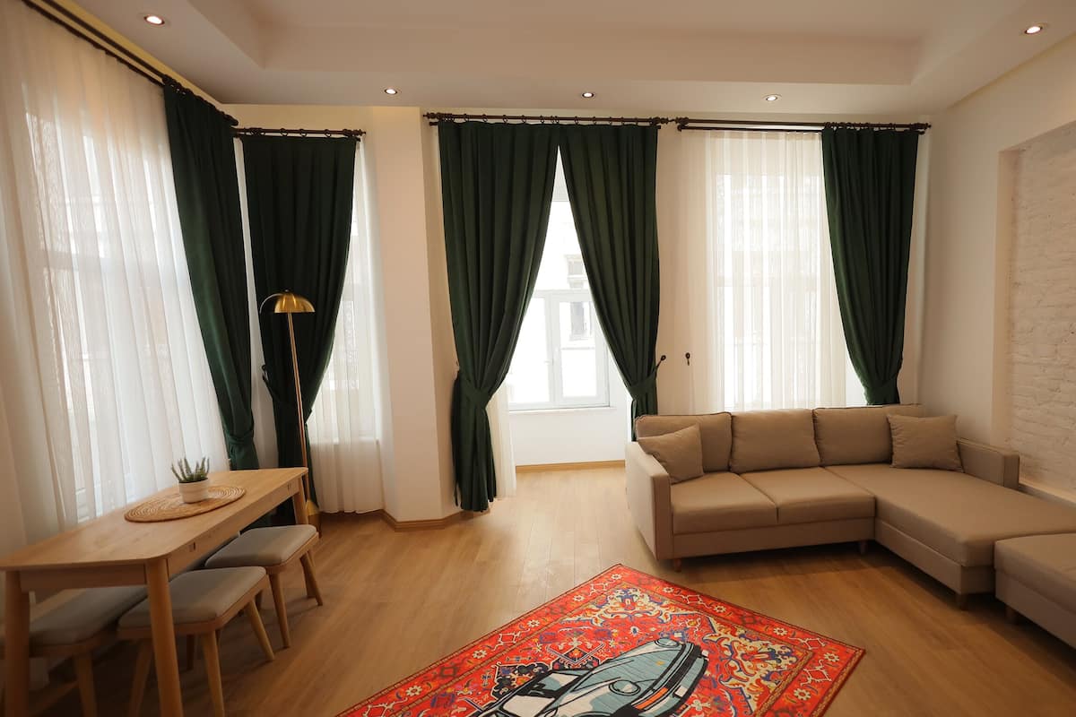 A modern living room with a sofa, a dining table with chairs, and a patterned rug.