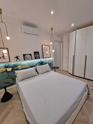 A modern bedroom with a large bed, a marble headboard, a wardrobe, and framed pictures on the wall.