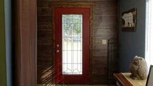 Una puerta de madera con marco rojo y un panel de cristal, una escultura de lechuza de piedra y un interruptor de luz fijado a la pared.