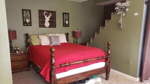 Un dormitorio con una cama de madera con dosel, una mesita de noche con lámpara y una escalera que lleva a un nivel superior.
