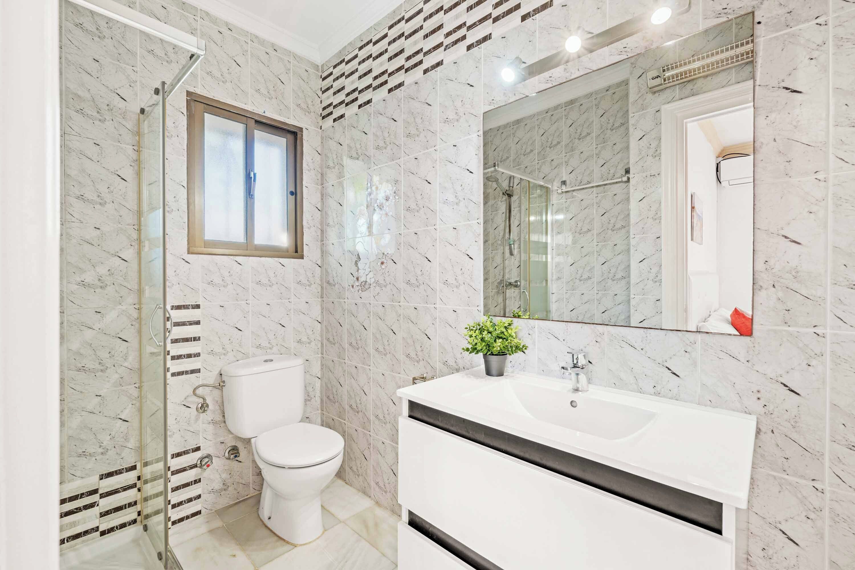 Un baño moderno con ducha envuelta en vidrio, inodoro y tocador blanco con espejo.