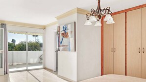 A bedroom with a bed, a chandelier, a wardrobe, and a sliding glass door leading to a balcony. - Villa Bart (Estepona)