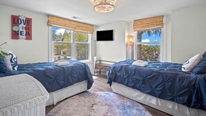 A bedroom with two beds, a TV, and large windows. - Ocean View Condo, Golf Cart Included, Private Patio, Newly Redecorated - 607 Newhaven (Fripp Island)