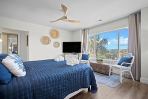 A bedroom with a bed, a TV, a ceiling fan, and a view of palm trees. - Ocean View Condo, Golf Cart Included, Private Patio, Newly Redecorated - 607 Newhaven (Fripp Island)
