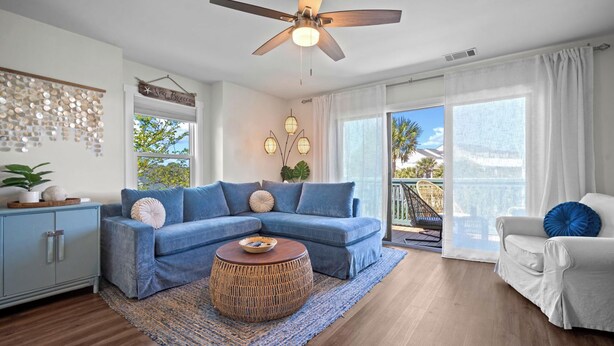 A living room with a blue sofa, a round coffee table, a ceiling fan, and a view of the outdoors. - Ocean View Condo, Golf Cart Included, Private Patio, Newly Redecorated - 607 Newhaven (Fripp Island)