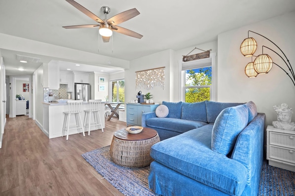 A modern living room with a blue sofa, a round wooden coffee table, and a ceiling fan. - Ocean View Condo, Golf Cart Included, Private Patio, Newly Redecorated - 607 Newhaven (Fripp Island)