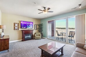 A living room with a fireplace, a television, a ceiling fan, and a view of the outdoors through a sliding glass door.