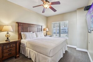 Un dormitorio con cama, mesitas de noche, lámparas, ventilador de techo y una ventana con persianas.