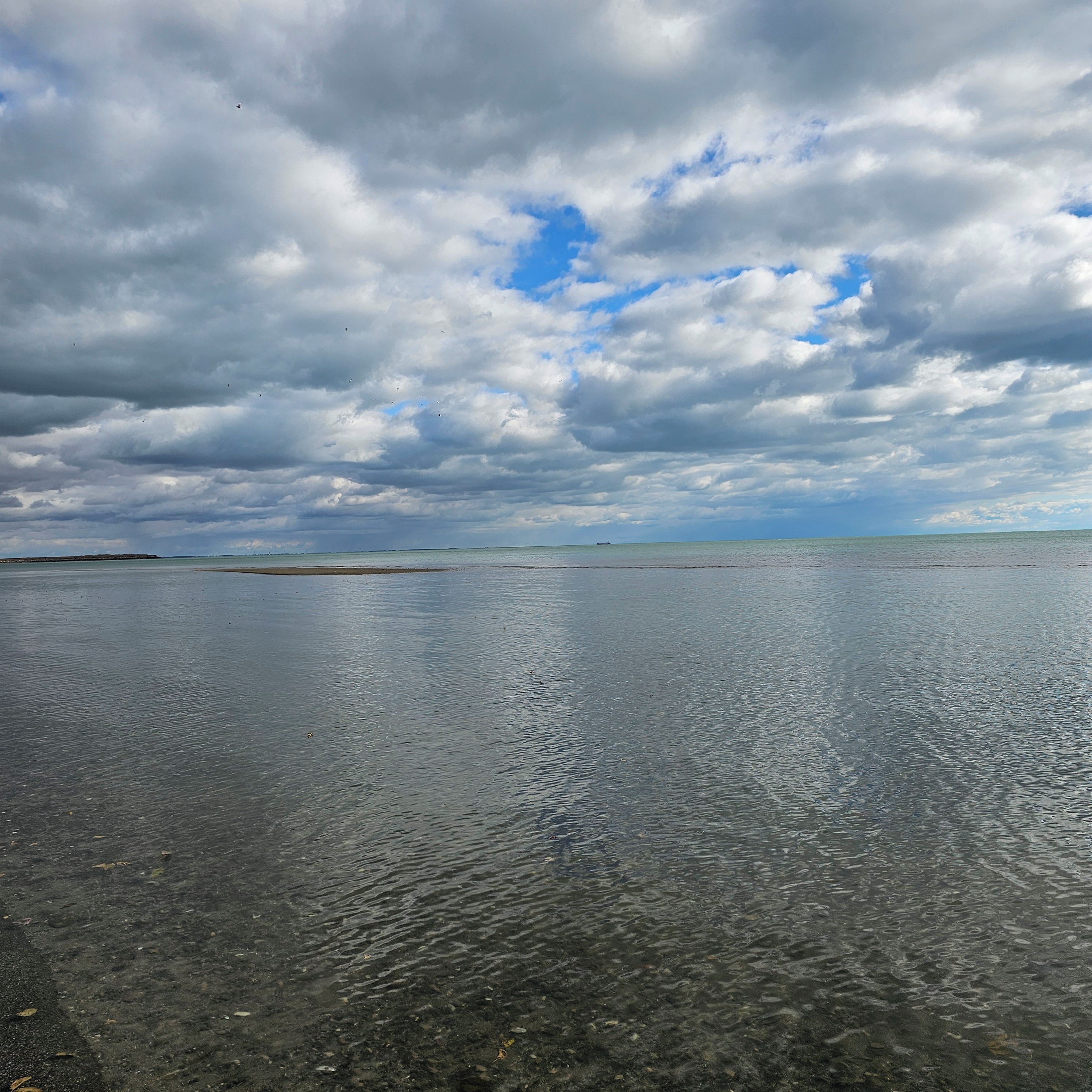 A beach with clear water and a cloudy sky.