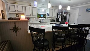 Une cuisine moderne avec des armoires blanches, un îlot central doté de tabourets de bar, un éclairage suspendu et une horloge au mur.
