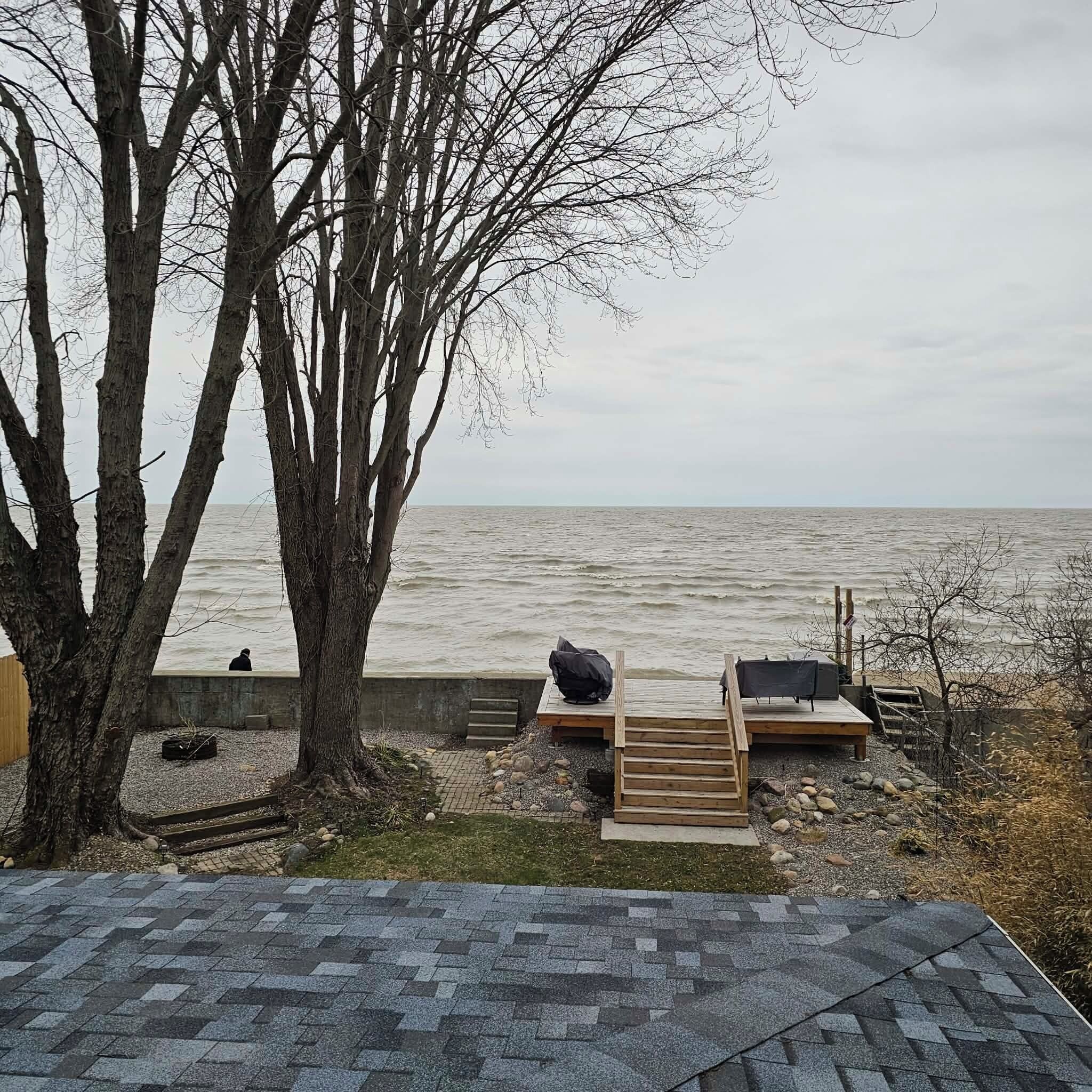 A view of a beach with a wooden deck, a bench, and a tree.