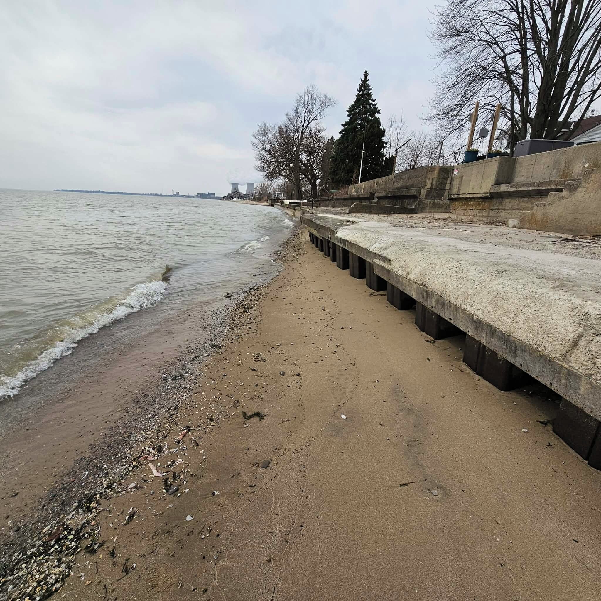 A concrete waterfront promenade with a sandy beach and a row of trees.