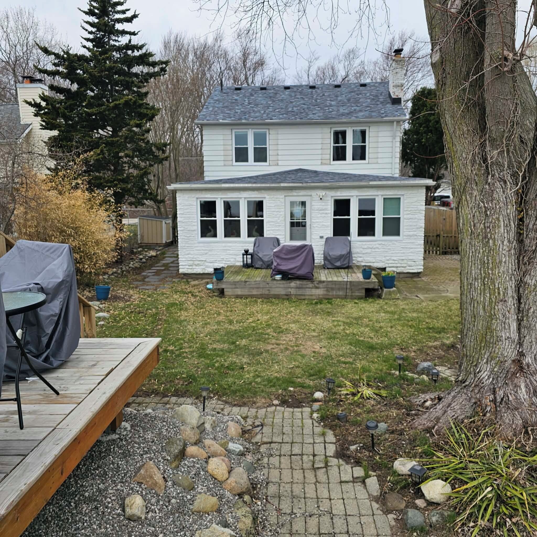 Et toetagers hus med en overdækket terrasse, en lille træterrasse og en have med en stenbelagt sti.