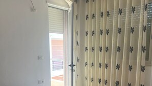 A hotel room with a large bed, white curtains with a floral pattern, and a view of a balcony.