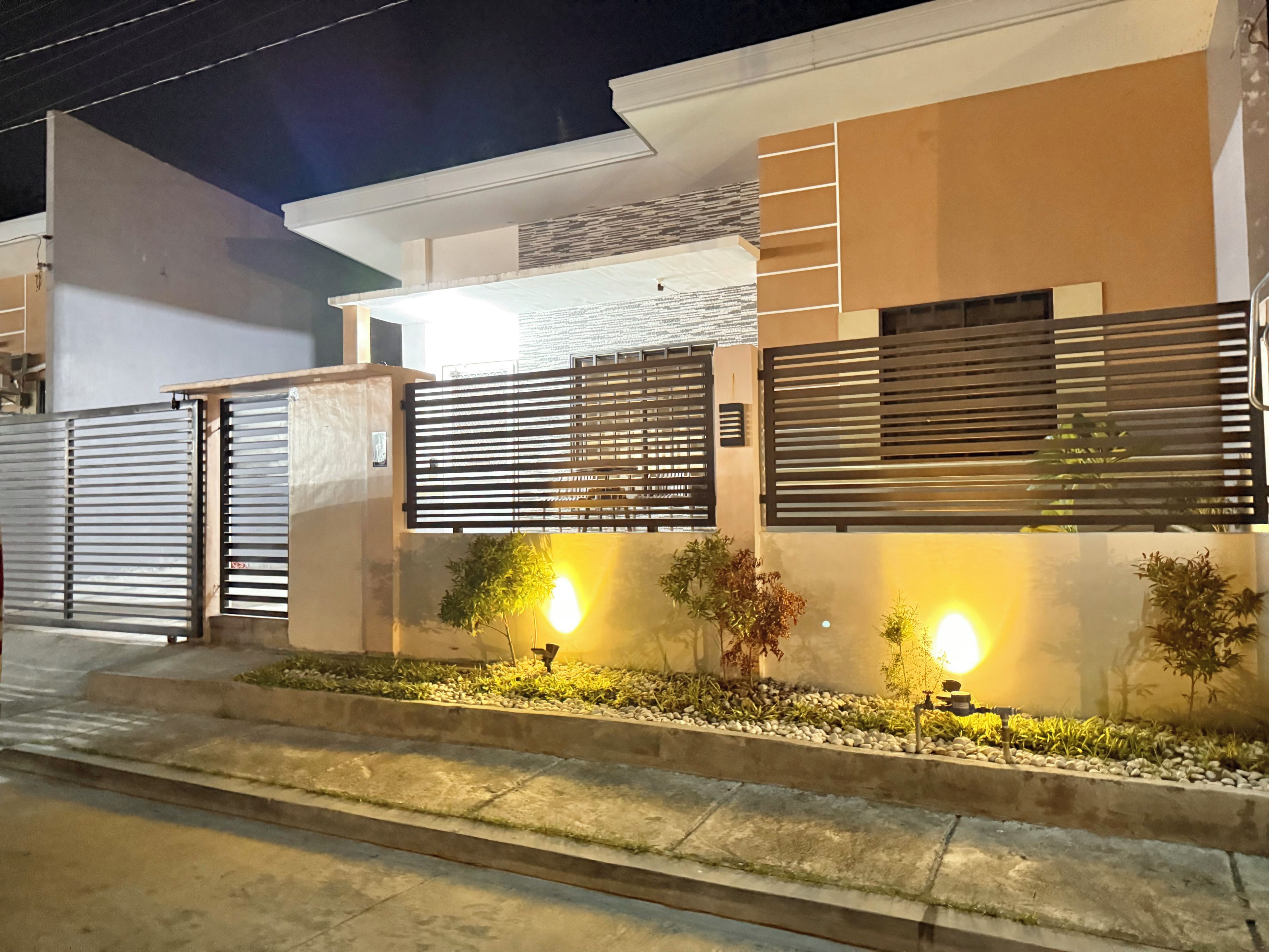 A modern house with a gated entrance, a well-lit pathway, and a small garden area.