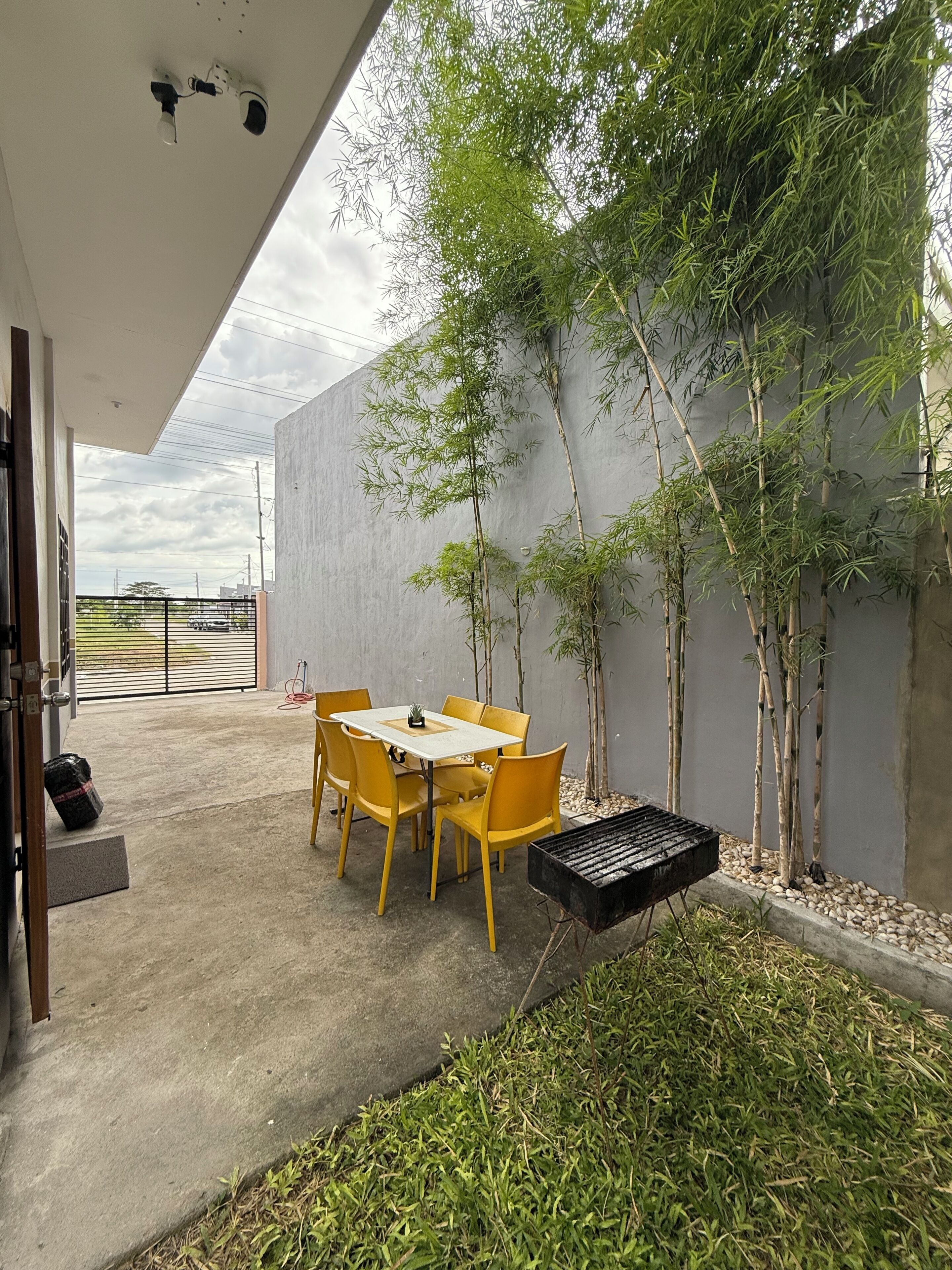 Een terras buiten met een tafel, stoelen, een barbecue en bamboeplanten.