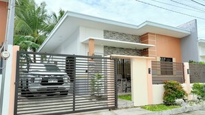 A modern two-story house with a gated entrance, a parked car, and a small garden area.