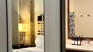 A hotel room with a bed, a bedside lamp, a large mirror, and a bathroom with a sink and toiletries. - Urban Style 2 BR | 2 Bath | Downtown | Free Valet Parking | 5 (Dallas)