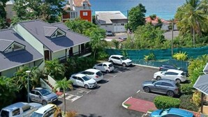 A parking lot with several cars, surrounded by buildings and palm trees, overlooking a body of water. - Apartment by the sea (Le Gosier)