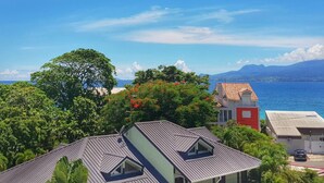 A coastal residential area with houses, a large tree, and a view of the sea and mountains. - Apartment by the sea (Le Gosier)