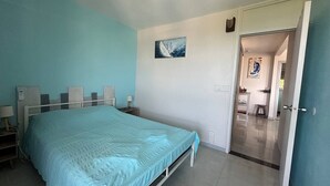A bedroom with a bed, bedside tables, a nightstand, a painting on the wall, and a door leading to another room. - Apartment by the sea (Le Gosier)